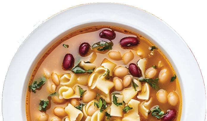 A bowl of soup with pasta, kidney beans, white beans, and herbs in a light broth.
