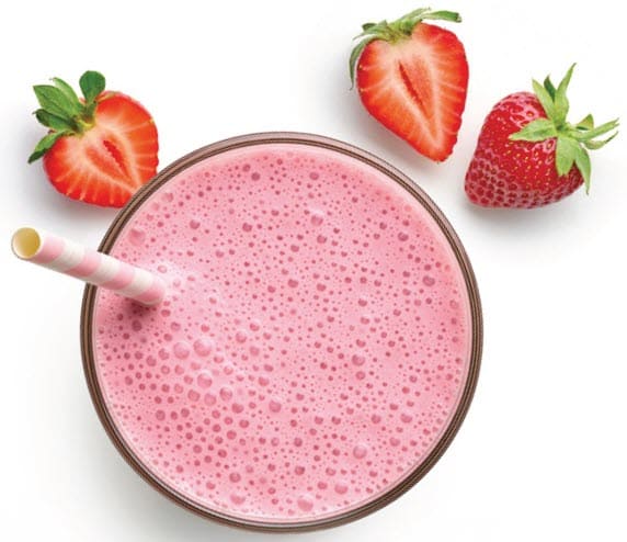 Top‑down view of a glass of pink strawberry smoothie with two striped straws and fresh strawberries around it.