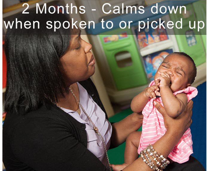 Adult holding a young baby in a playroom, comforting the baby while being picked up.