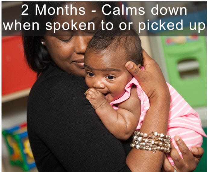 Adult holding a young baby in a playroom, comforting the baby while being picked up.
