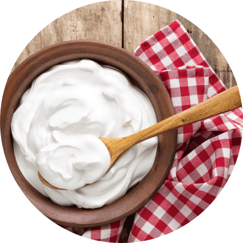 Bowl of thick white yogurt with a wooden spoon on a red‑and‑white checkered cloth.